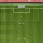 A stark top-down view of a completely empty football pitch, emphasizing the geometric lines of the penalty area.