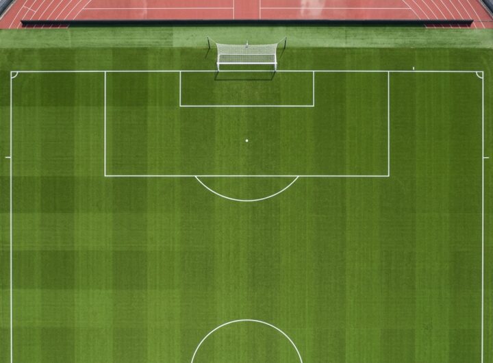 A stark top-down view of a completely empty football pitch, emphasizing the geometric lines of the penalty area.