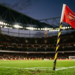 A low angle shot of a pristine corner flag at the Emirates Stadium with blurred stadium lights in the background.