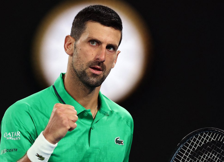 A low angle shot of a tennis racket casting a long shadow on a purple hard court surface.