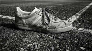 A close-up view of a worn tennis shoe heavily planted on a highly textured hard court, captured in stark monochrome.