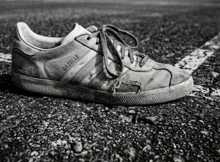 A close-up view of a worn tennis shoe heavily planted on a highly textured hard court, captured in stark monochrome.